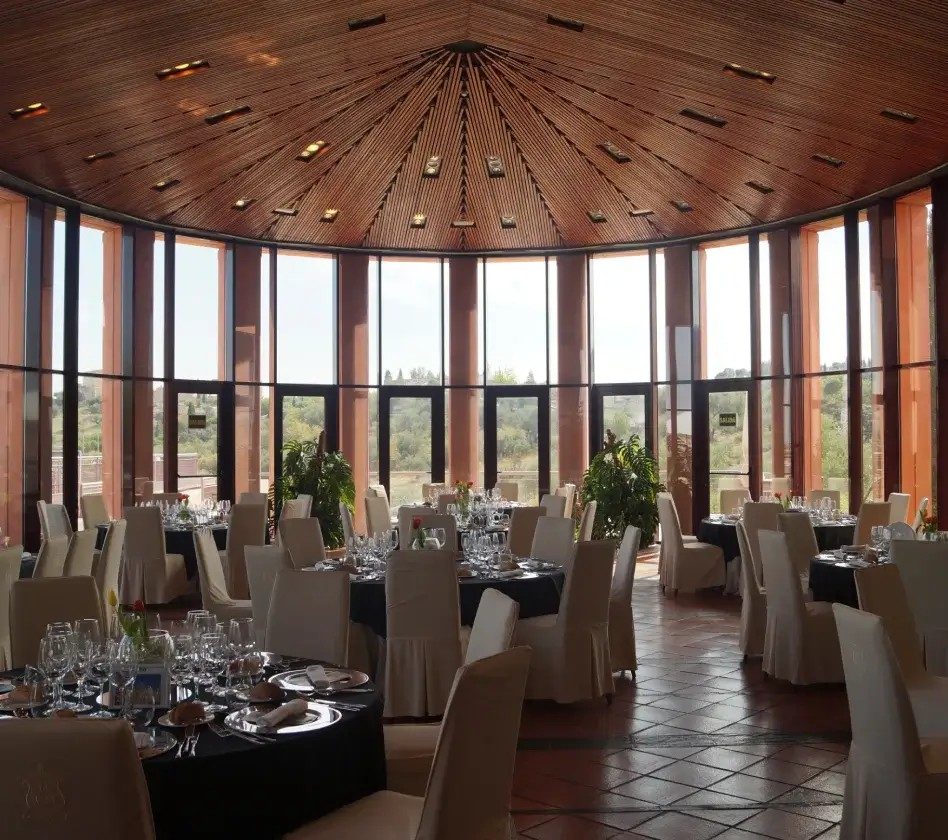Salón circular con techo de madera montado con mesas redondas y manteles blancos