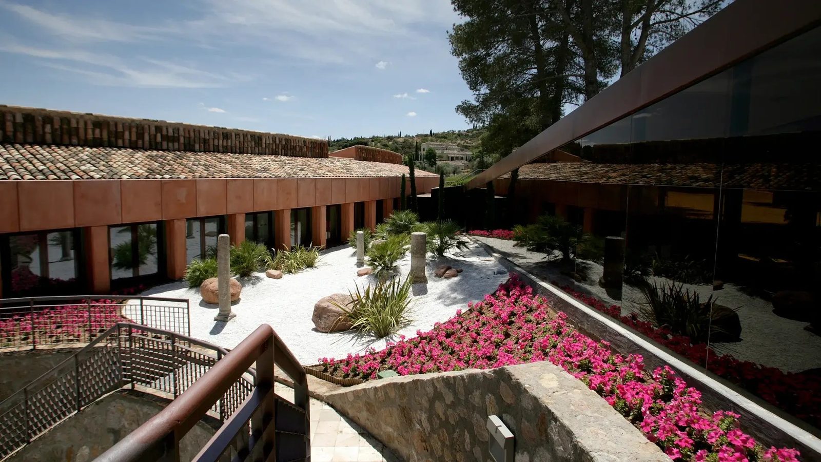 Patio con jardín de grava blanca, plantas y flores, y el edificio del cigarral