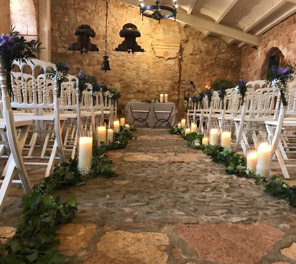 Pasillo de ceremonia con velas y flores en un espacio de piedra