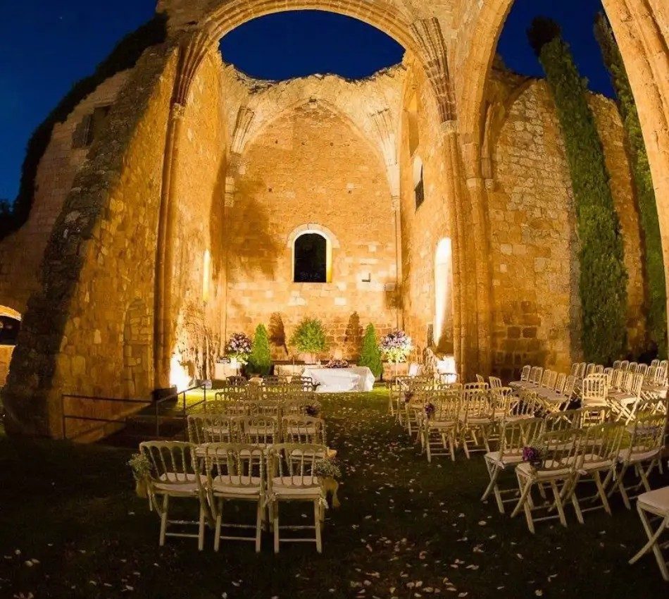 Ceremonia al aire libre en las ruinas iluminadas, con sillas y decoración floral