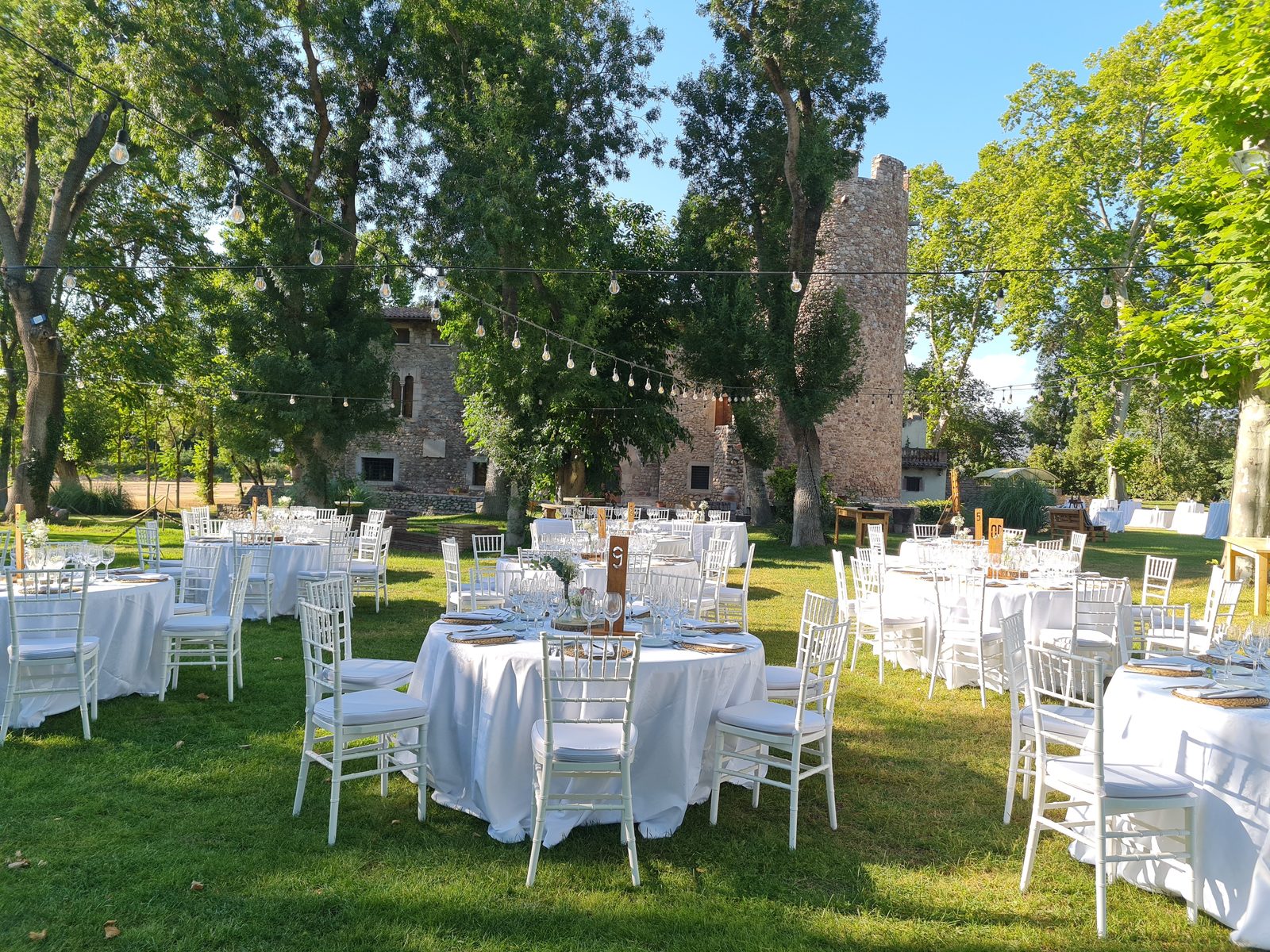 Montaje de comedor para banquete de boda al exterior, en el jardín central, con mesas blancas y el castillo de fondo